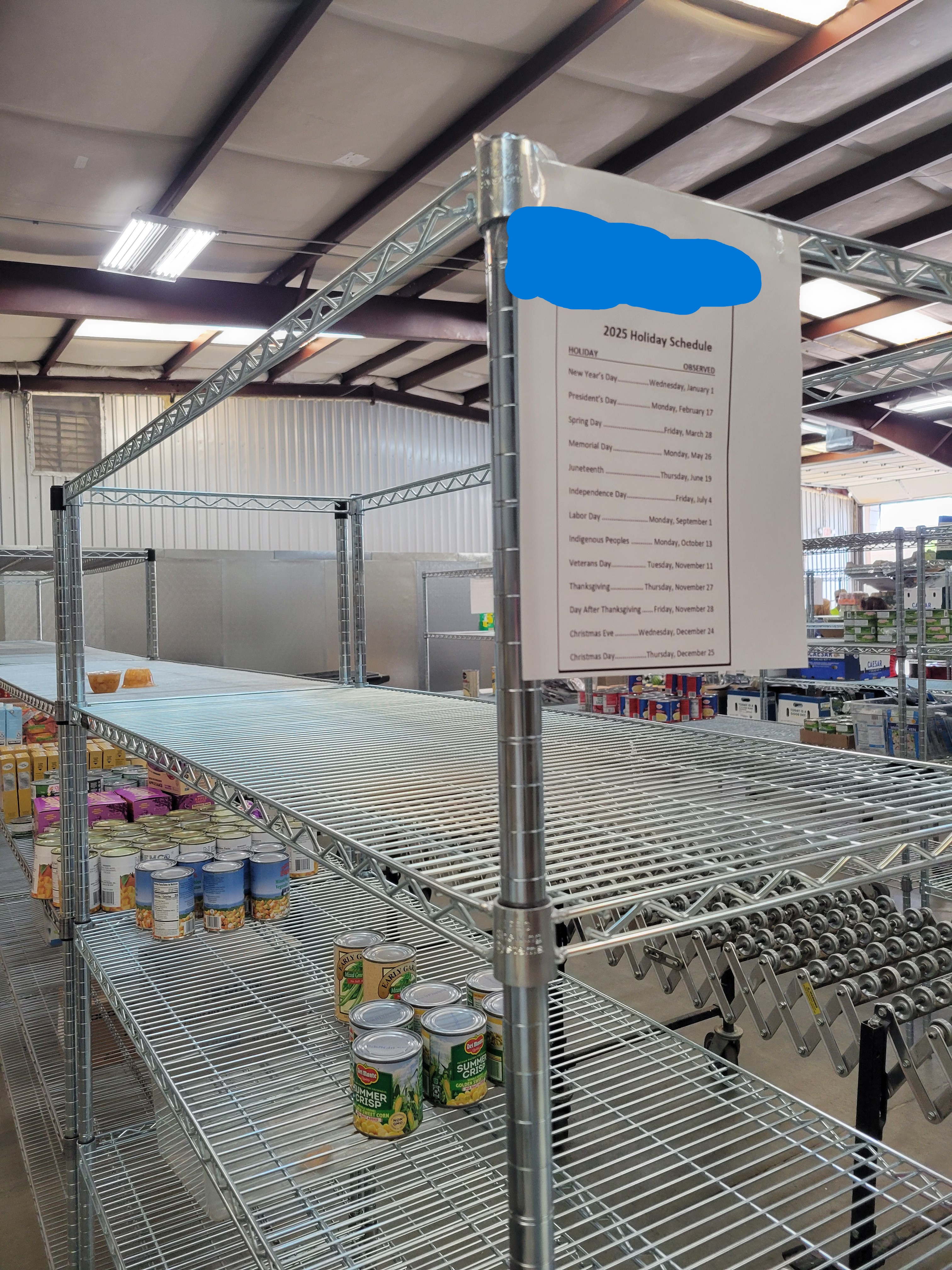 Shelf with cans and a sign listing 2025 food bank holidays.